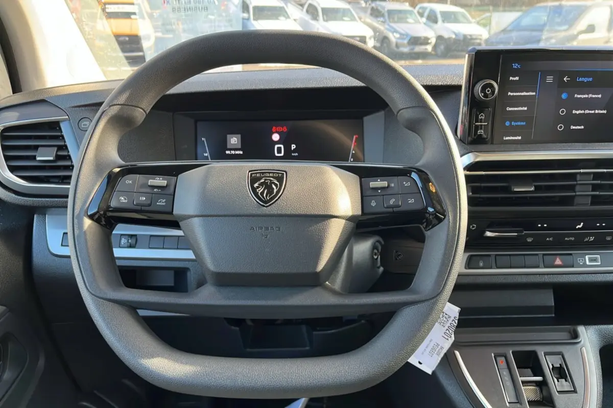 Vue intérieure centrée sur le volant multifonctions et les écrans digitaux du Peugeot Traveller gris acier 2025.