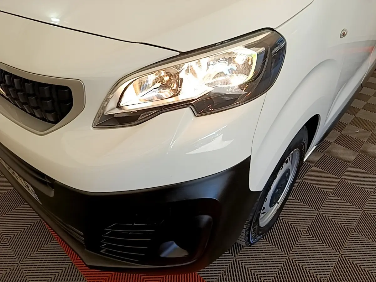 Gros plan sur l’avant droit du Peugeot Traveller blanc de 2018, avec phare allumé et pare-chocs noir mat.