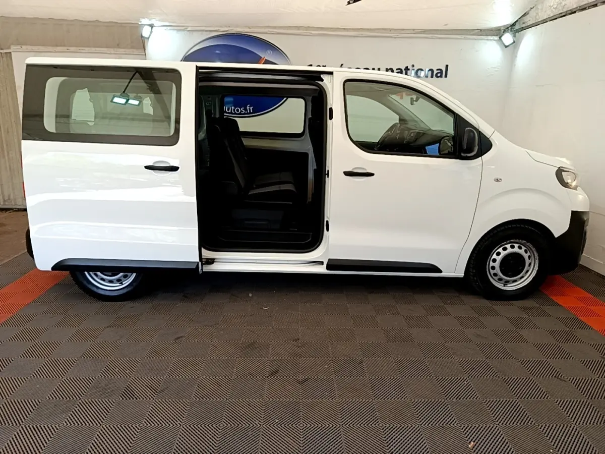 Vue latérale droite d'un Peugeot Traveller blanc 2018 avec porte coulissante ouverte, intérieur visible et jantes acier noires.