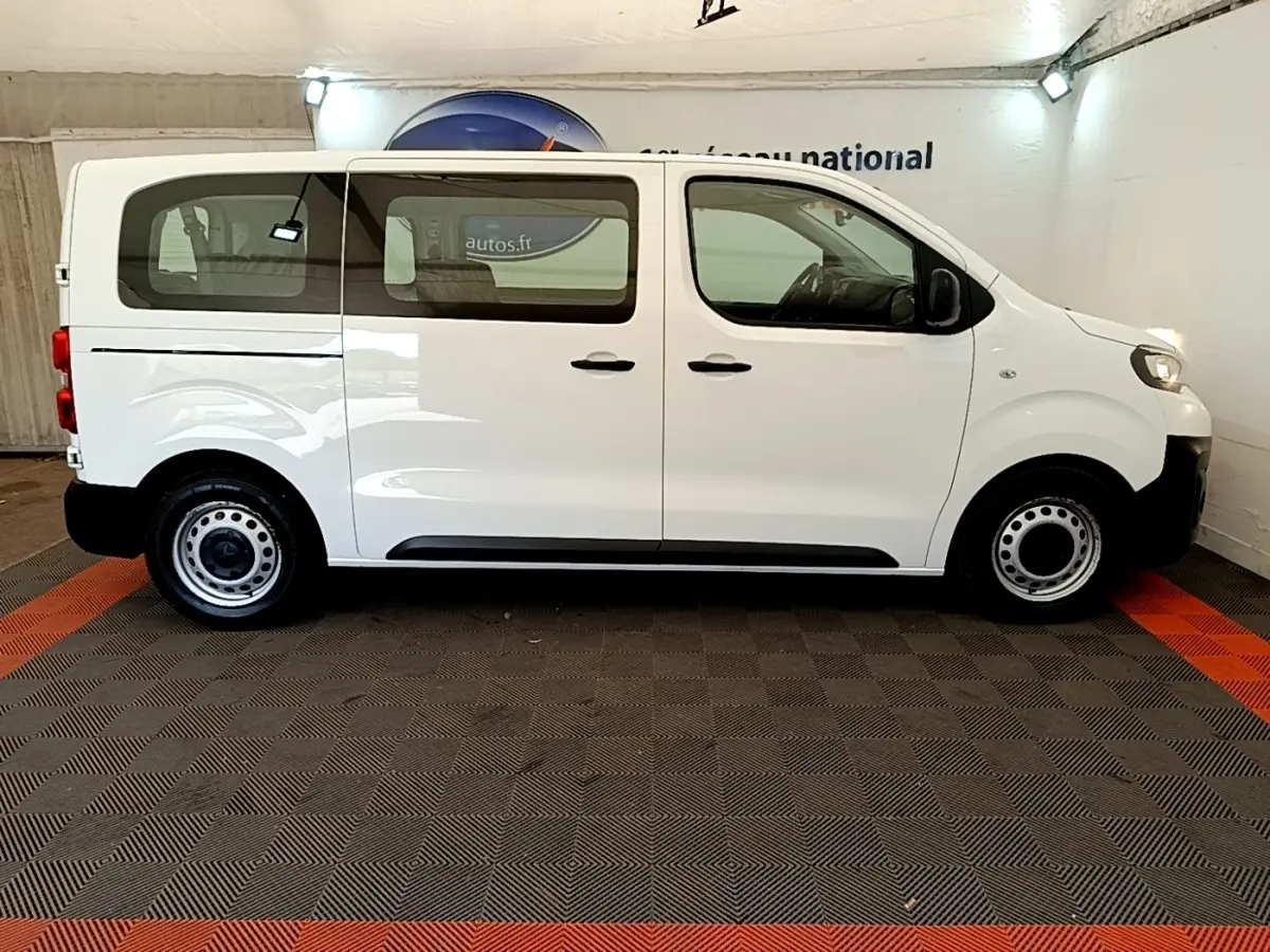 Vue de profil côté gauche d’un Peugeot Traveller blanc de 2018 avec jantes acier et vitres teintées arrière.