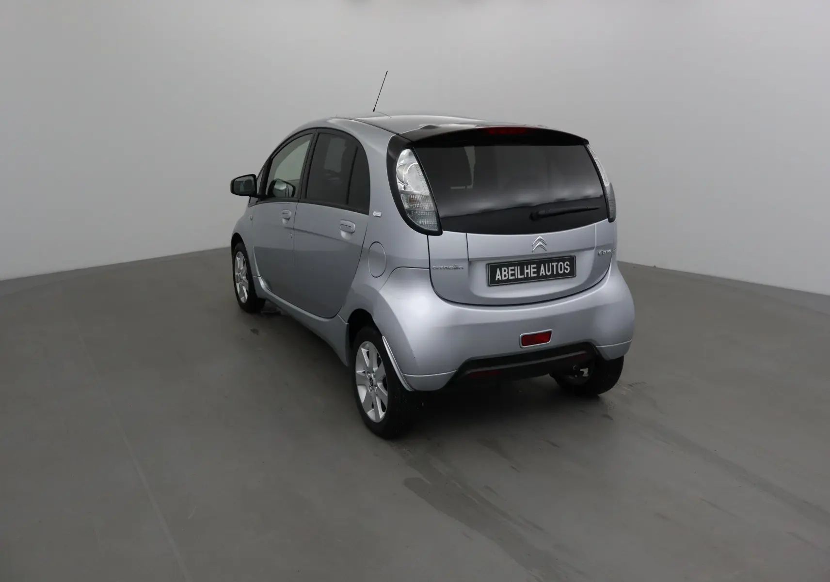Vue 3/4 arrière droite d'une Citroën C-ZERO gris alu 2018 avec vitres arrière teintées et plaque Abeilhe Autos.