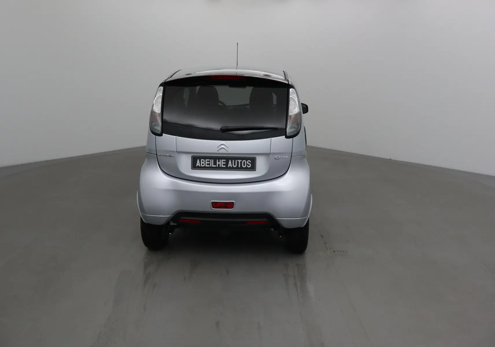 Vue arrière d'une Citroën C-Zero gris alu 2018, compacte et électrique, avec vitres arrière teintées et plaque Abeilhe Autos.