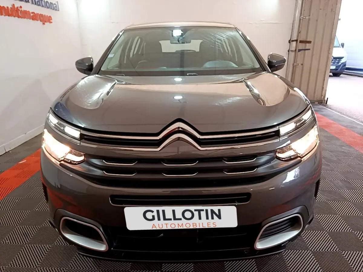 Vue avant d'un Citroën C5 Aircross gris foncé avec feux allumés et calandre chromée dans un garage.