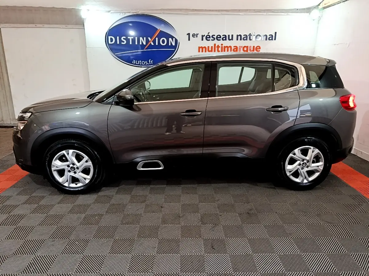 Profil côté gauche du SUV Citroën C5 Aircross gris foncé avec jantes alliage 17 pouces en intérieur showroom.