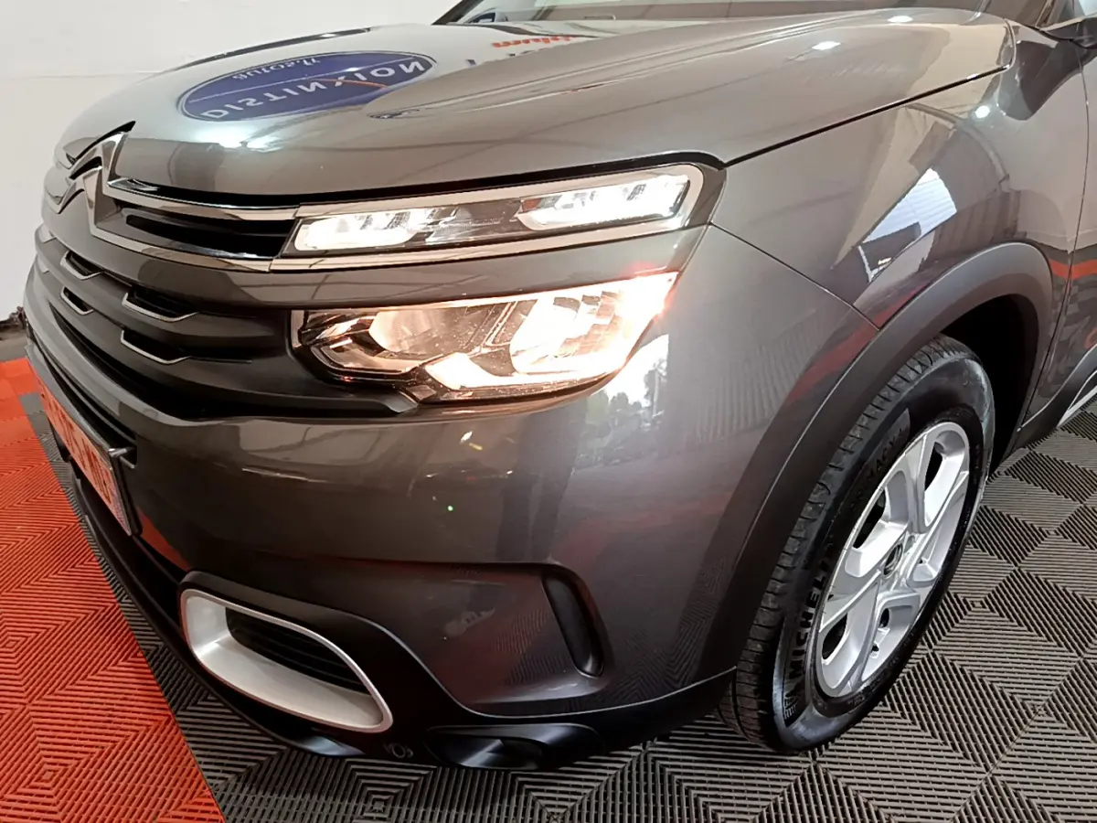 Vue 3/4 avant droit du Citroën C5 Aircross gris foncé avec feux allumés et jantes alliage 17 pouces.