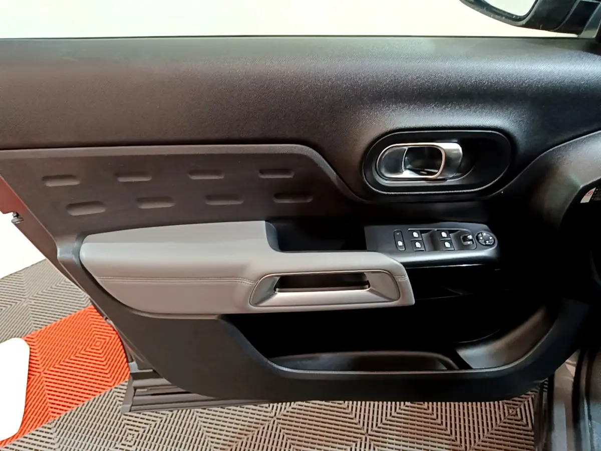 Gros plan sur la porte côté gauche du Citroën C5 Aircross gris foncé, avec accoudoir gris clair et commandes électriques.