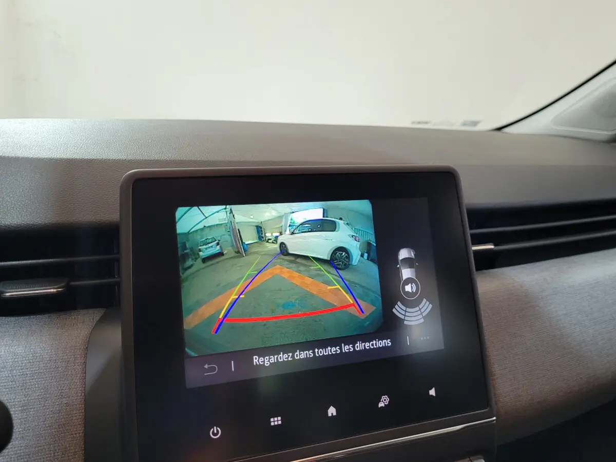 Écran tactile central montrant la caméra de recul d’une Renault Clio gris foncé en stationnement intérieur.