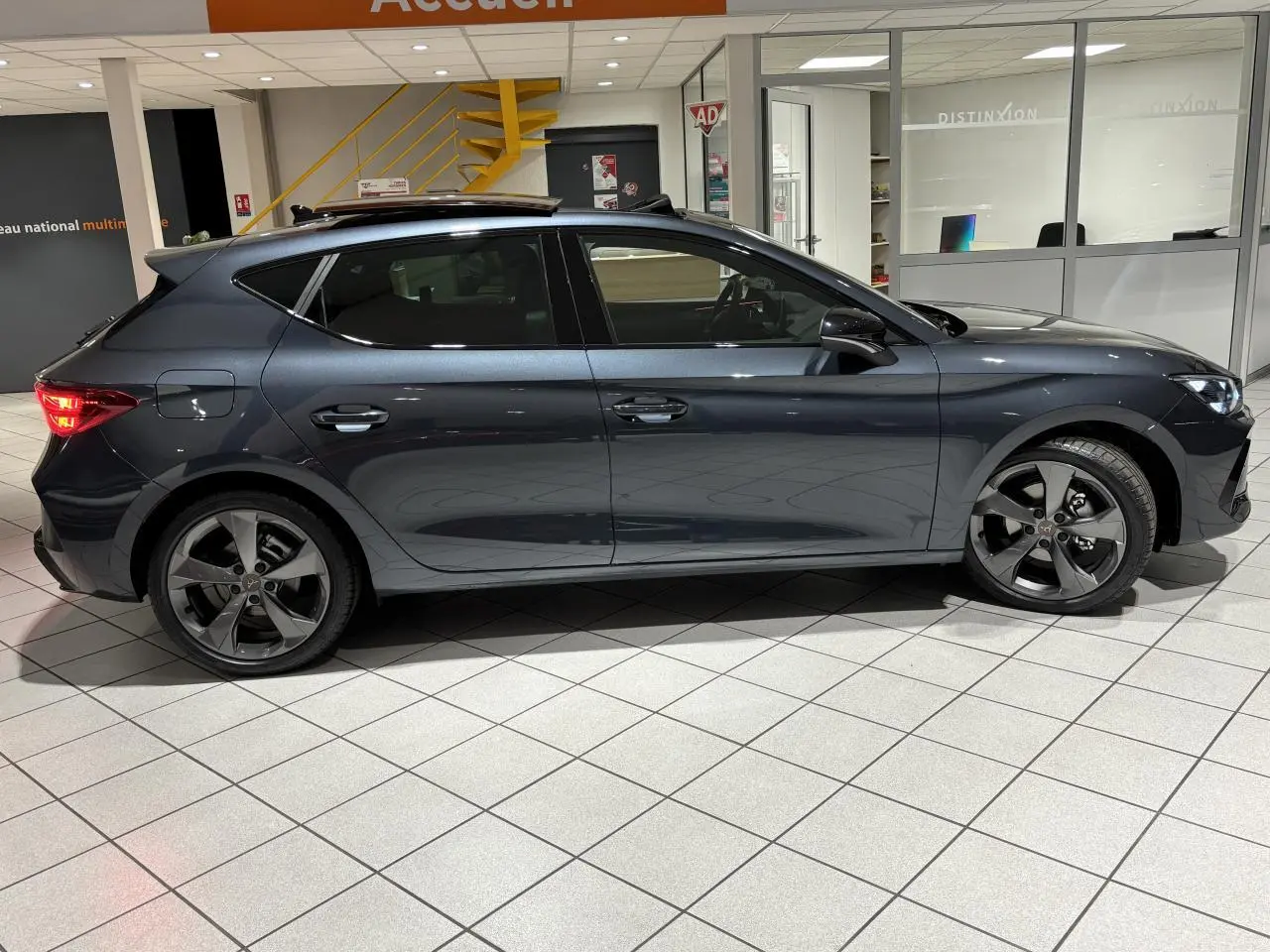 Vue de profil côté gauche d'une CUPRA Leon gris Graphène avec jantes alliage 18 pouces et toit ouvrant panoramique.