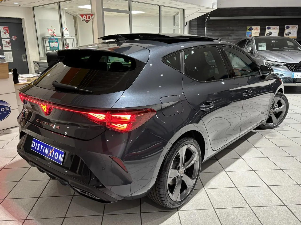 Vue 3/4 arrière droite d'une CUPRA Leon gris Graphène avec feux arrière Tri-LED et toit ouvrant panoramique.
