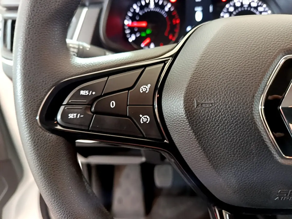 Gros plan sur le volant noir du Renault Trafic Fourgon 2022 avec commandes de régulateur de vitesse et tableau de bord flou.