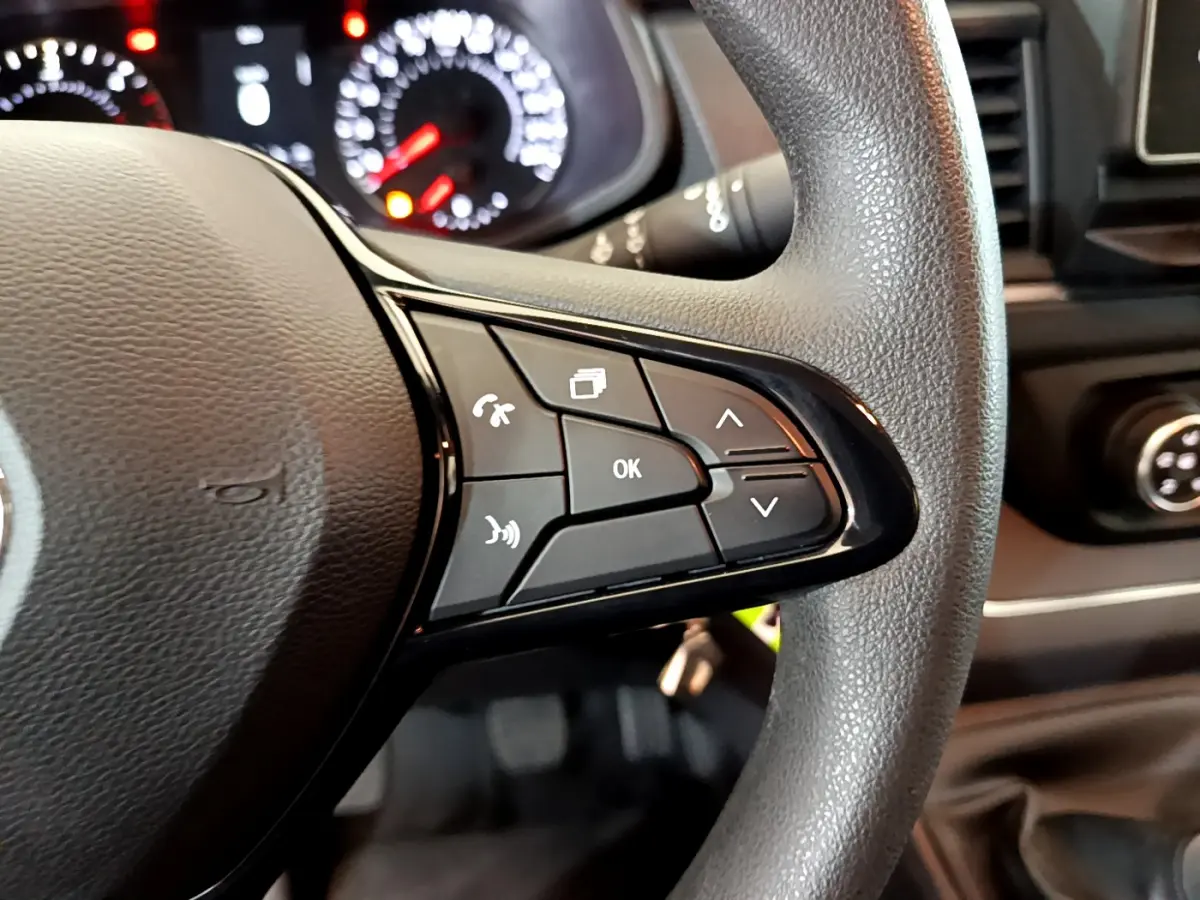 Gros plan sur les commandes multifonctions du volant noir du Renault Trafic Fourgon 2022, avec tableau de bord en arrière-plan flou.