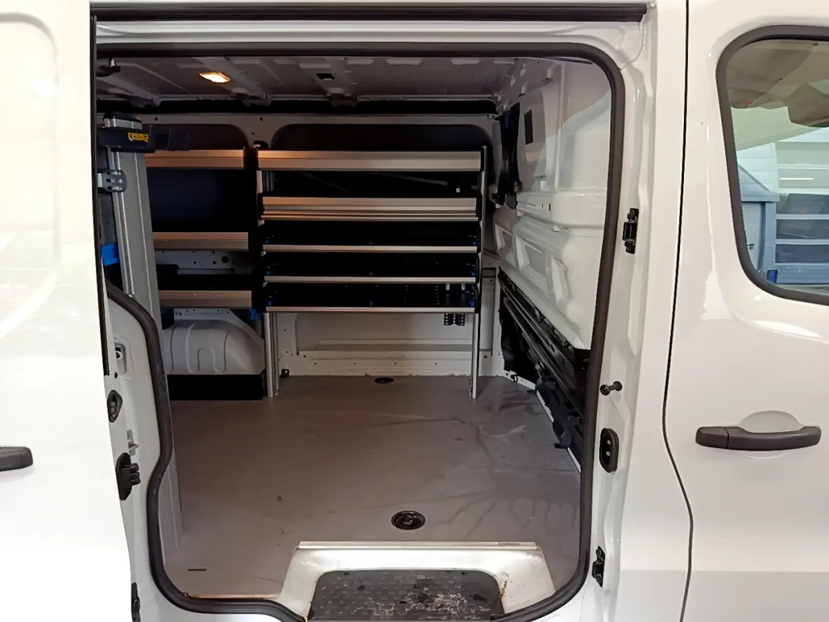 Vue intérieure du Renault Trafic Fourgon blanc 2022, montrant l'espace de chargement avec étagères métalliques sur le côté gauche.