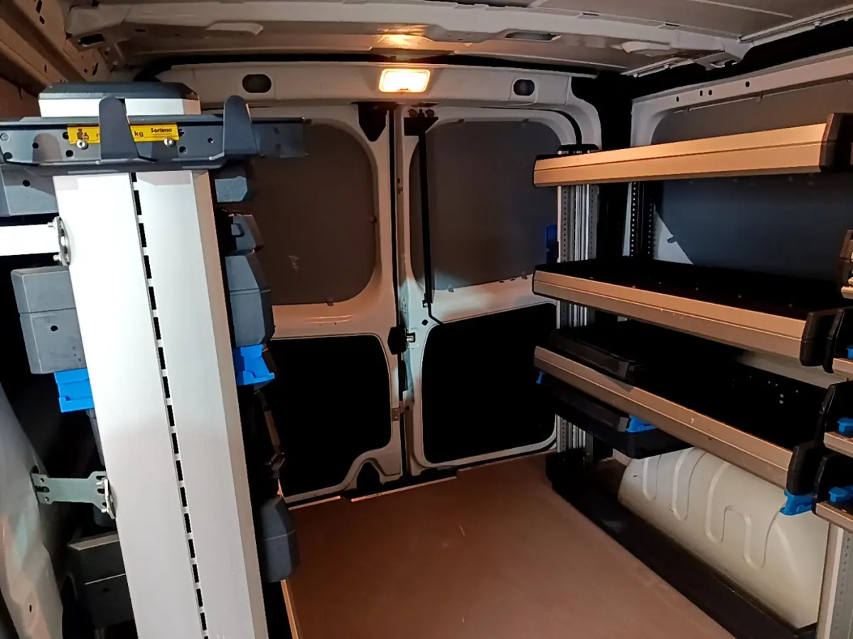 Intérieur du fourgon blanc Renault Trafic FG CF L1H1 2022, vue arrière avec étagères de rangement et cloison pleine.