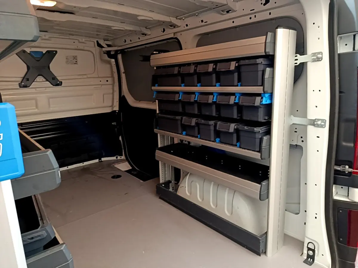 Intérieur du fourgon Renault Trafic blanc vu de l'arrière, avec étagères et rangements modulaires sur le côté droit.