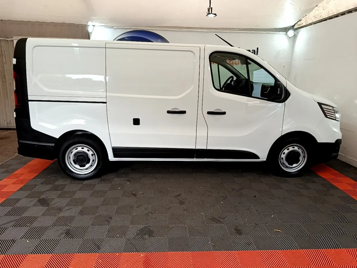 Profil côté gauche d'un fourgon Renault Trafic blanc, avec jantes acier et détails noirs contrastants.