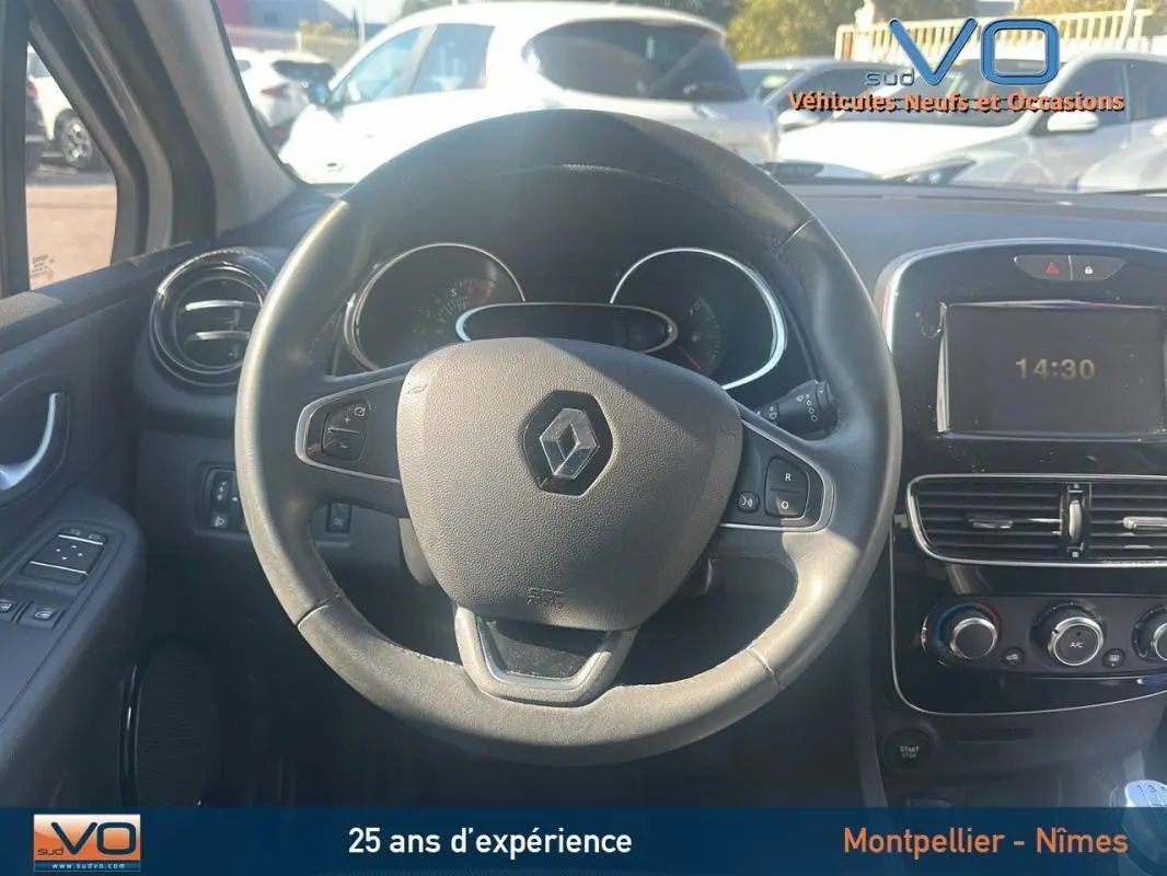 Vue intérieure centrée sur le volant cuir de la Renault Clio IV Estate Business blanche, avec tableau de bord et commandes visibles.
