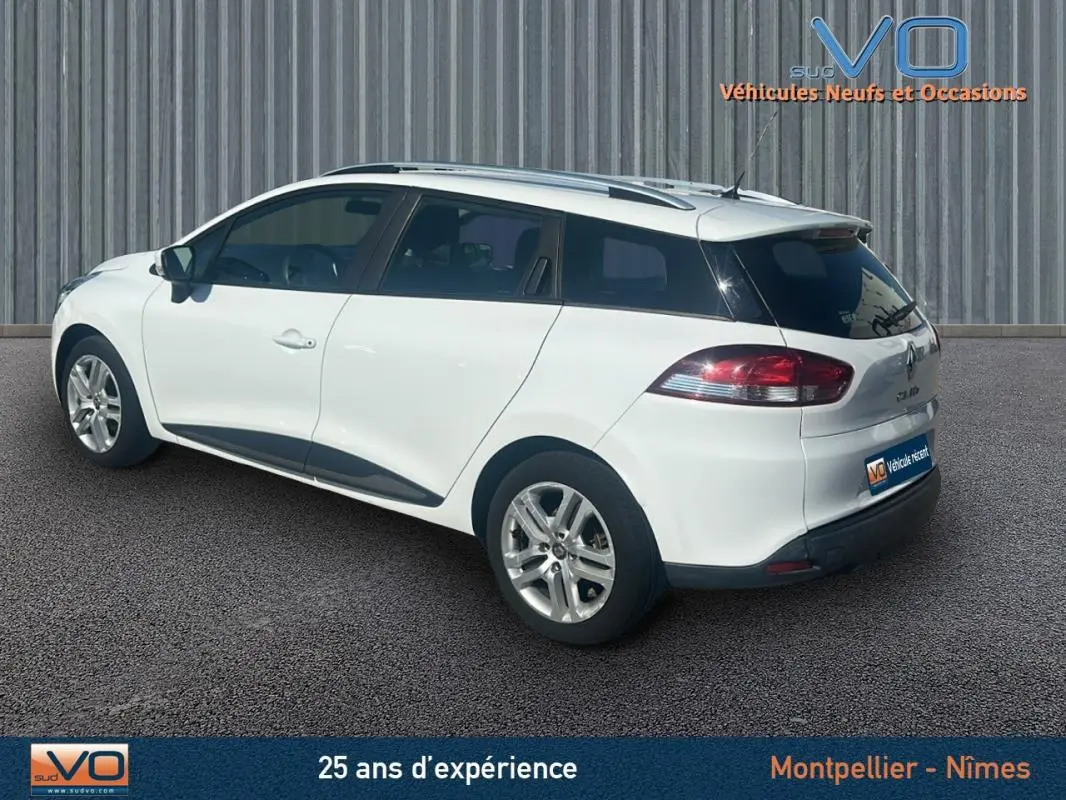 Vue 3/4 arrière droite d'une Renault Clio IV Estate Business blanche avec vitres surteintées et barres de toit.