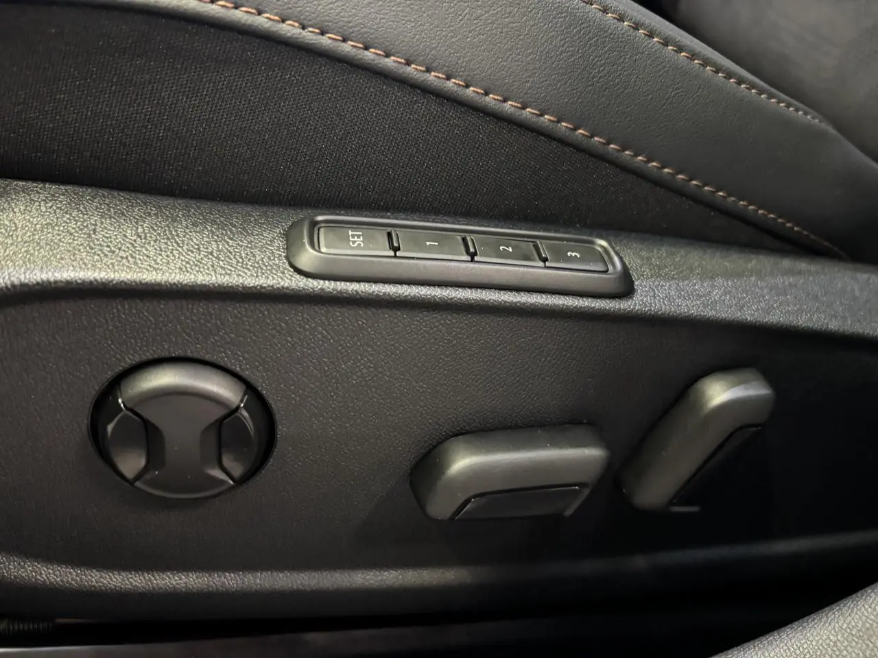 Détail des commandes de réglage électrique du siège conducteur noir avec surpiqûres cuivrées sur une CUPRA Leon Bleu Fjord.