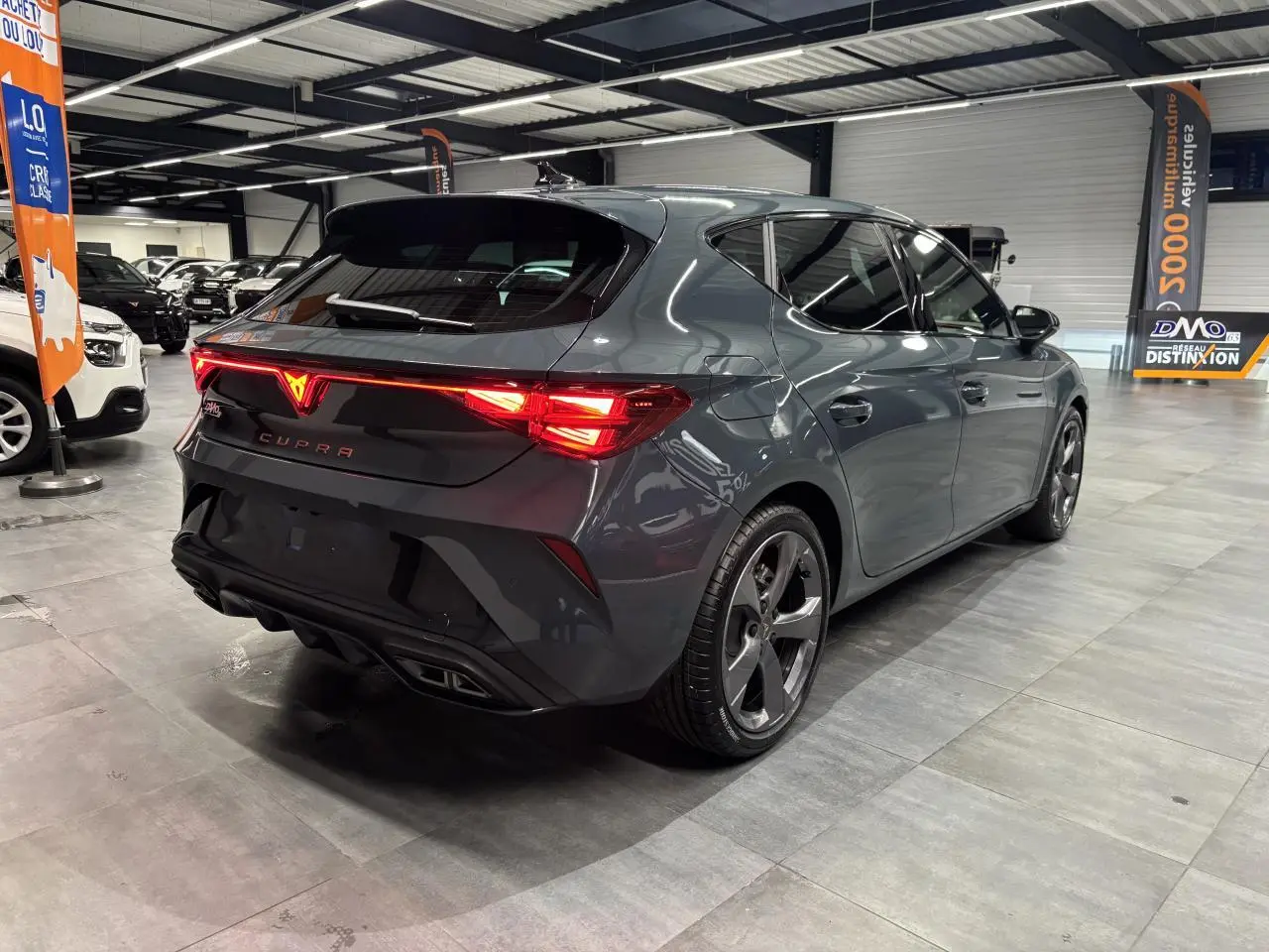 Vue 3/4 arrière droite d'une CUPRA Leon bleu Fjord avec feux arrière Tri-LED et double sortie d'échappement noire.