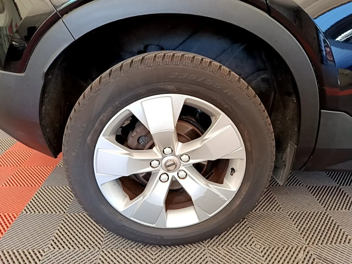 Gros plan sur la roue avant droite d’un Volvo XC40 noir, jante alliage argentée avec logo Volvo au centre.