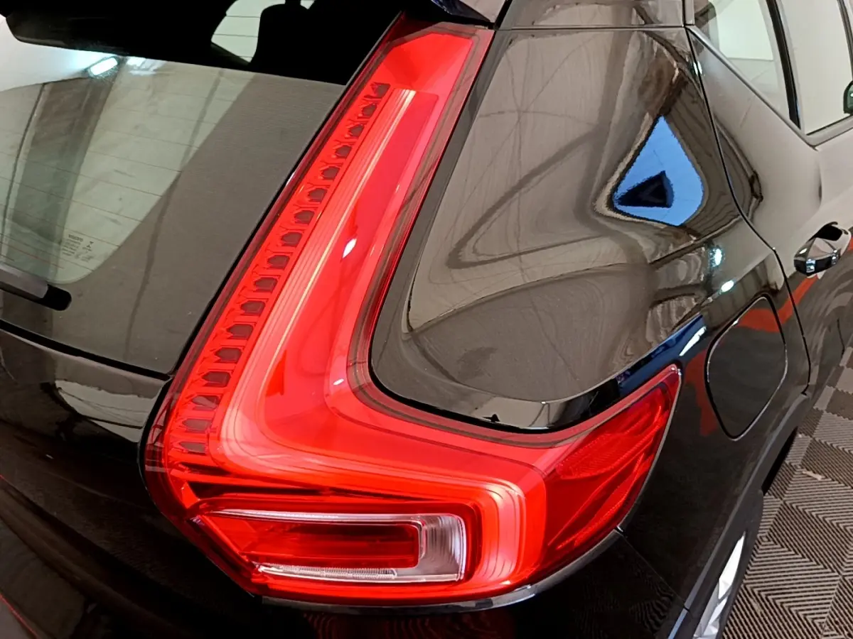 Gros plan sur le feu arrière gauche rouge vif d’un Volvo XC40 noir, mettant en valeur la carrosserie brillante.