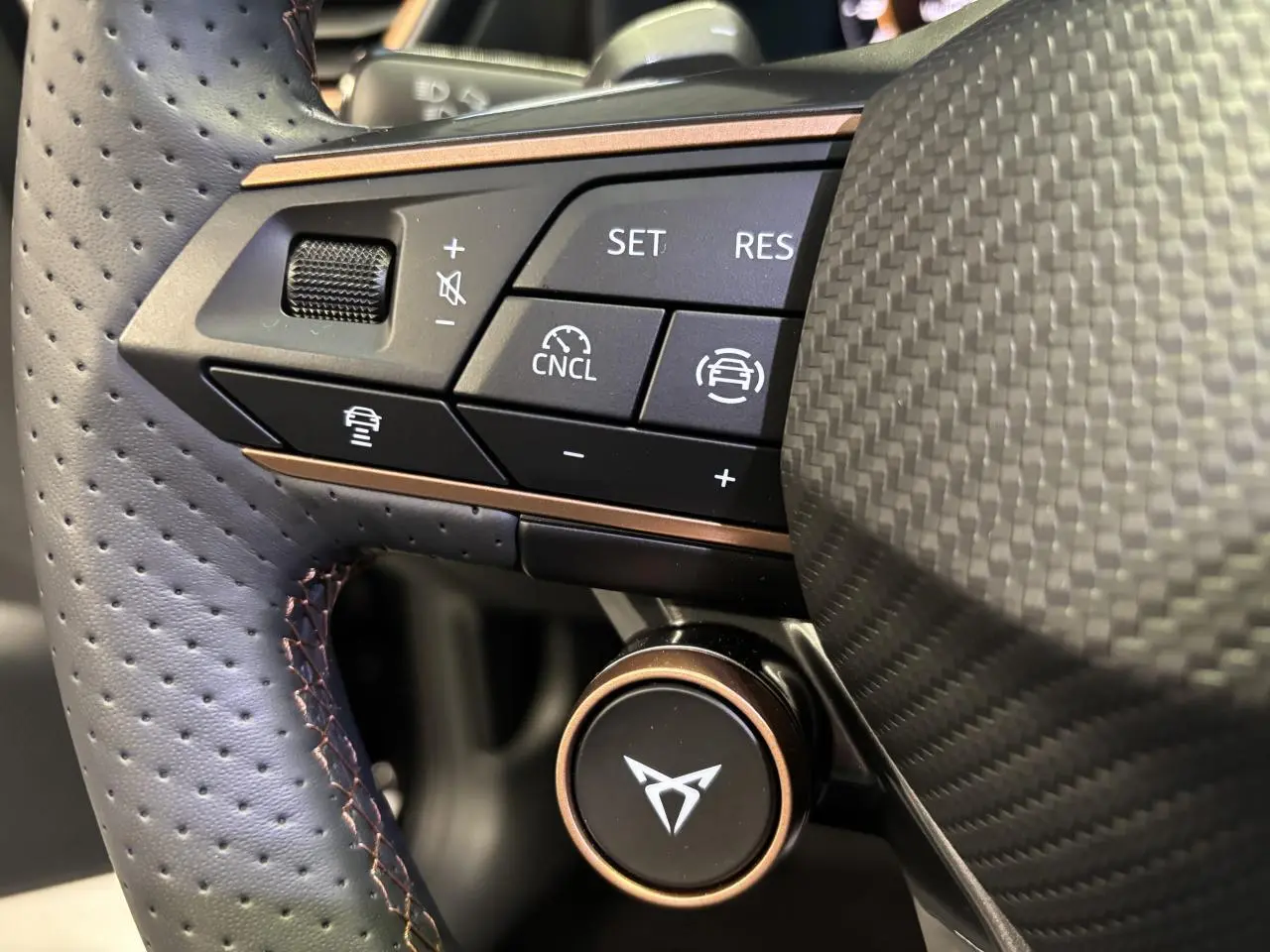 Gros plan sur le volant perforé noir avec surpiqûres cuivrées et commandes multifonctions du CUPRA Leon gris Magnetic.