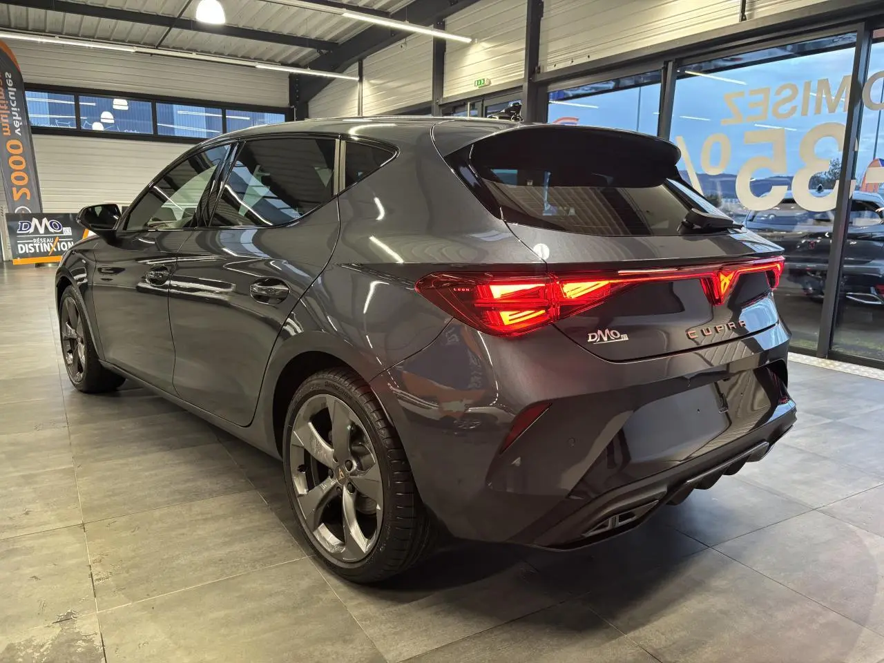 Vue 3/4 arrière droite d'une CUPRA Leon gris magnetic avec feux arrière Tri-LED et jantes anthracite 18 pouces.