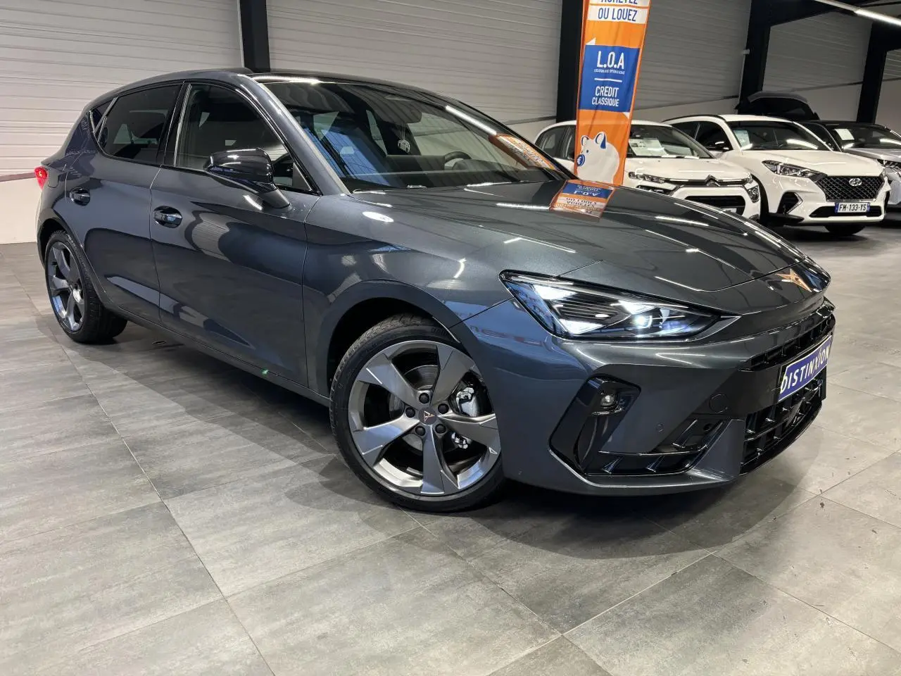 Vue 3/4 avant droite d'une CUPRA Leon gris magnetic avec jantes alliage 18 pouces et phares LED allumés.