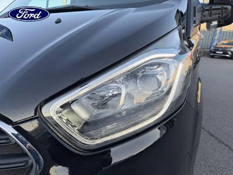 Gros plan sur le phare avant droit du Ford Transit Custom noir Agate métallisé, mettant en valeur son design moderne et précis.