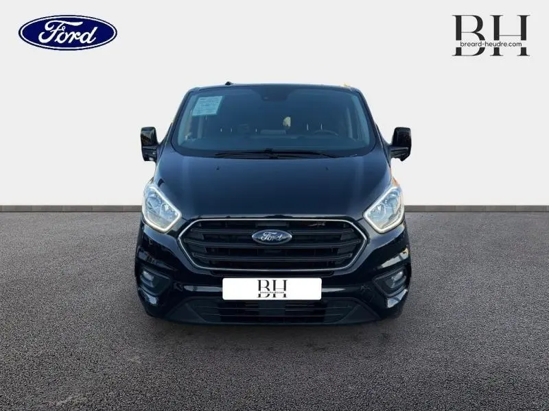 Vue de face du Ford Transit Custom Fourgon noir Agate métallisé avec calandre chromée et phares allumés.