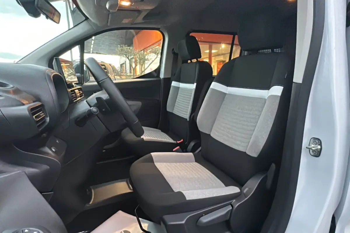 Vue intérieure côté conducteur du Citroën Berlingo 2025, sièges tissu gris et noir avec volant multifonctions.