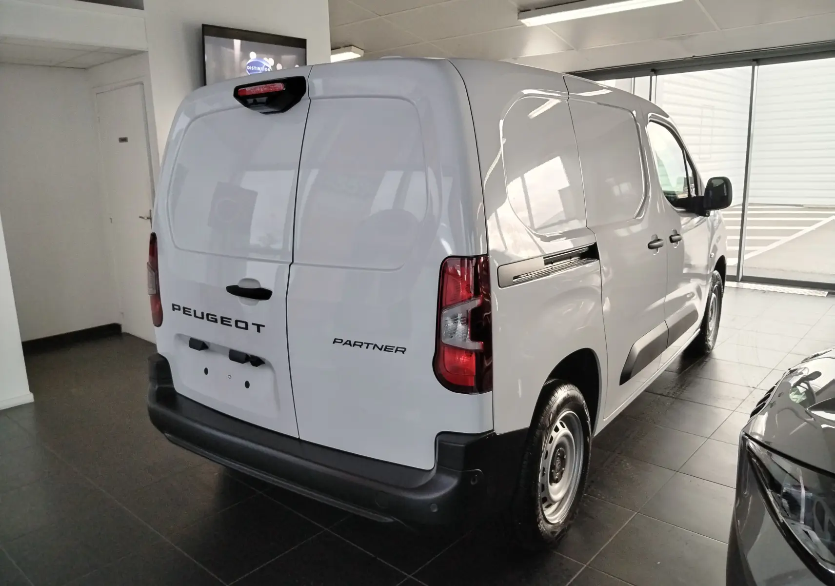 Vue 3/4 arrière droite du Peugeot Partner FGN blanc Icy 2025 en showroom, avec portes arrière fermées et feux rouges visibles.
