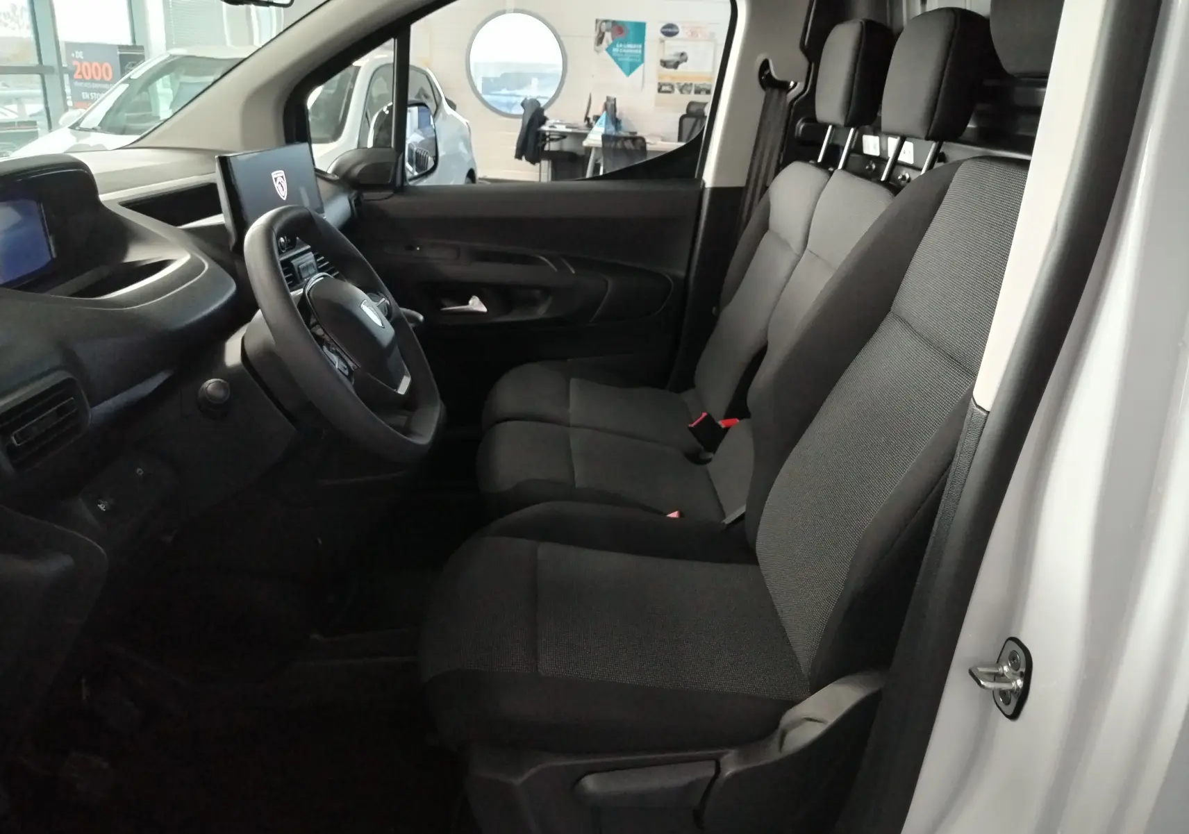 Vue intérieure côté conducteur du Peugeot Partner FGN blanc Icy 2025, montrant les sièges avant et le tableau de bord avec écran numérique.