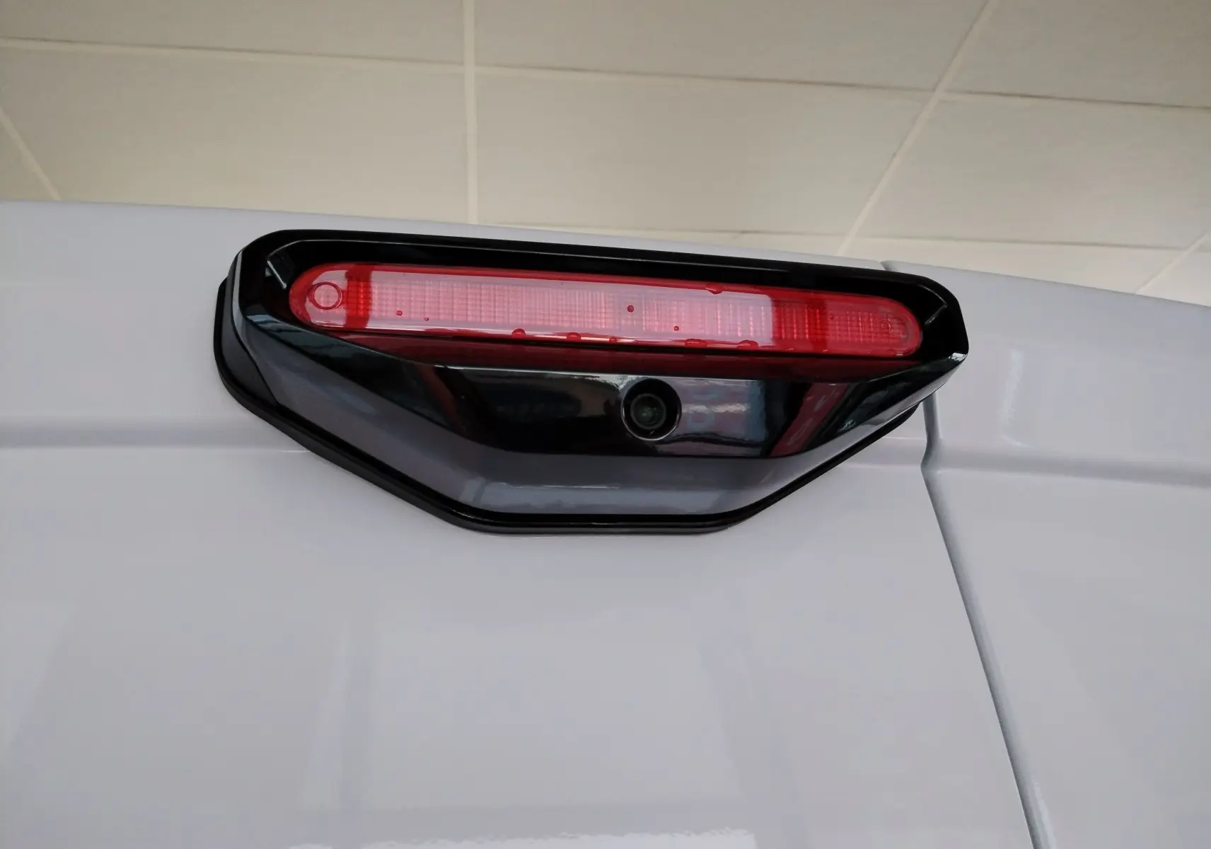 Gros plan sur le feu stop arrière rouge avec caméra intégrée du Peugeot Partner FGN blanc Icy, vue arrière haute.