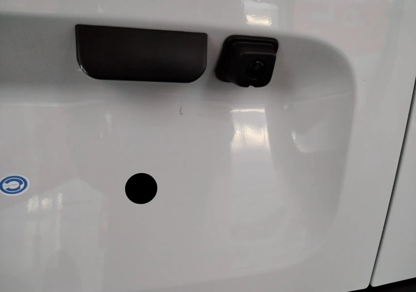 Gros plan sur la poignée et la caméra de recul noire sur la porte arrière blanche du Peugeot Partner FGN 2025.