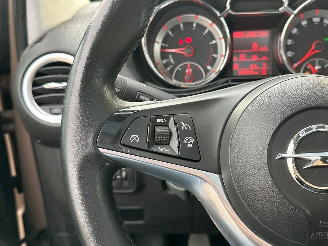 Gros plan sur le volant cuir de l'Opel Adam marron, mettant en valeur les commandes du régulateur de vitesse.