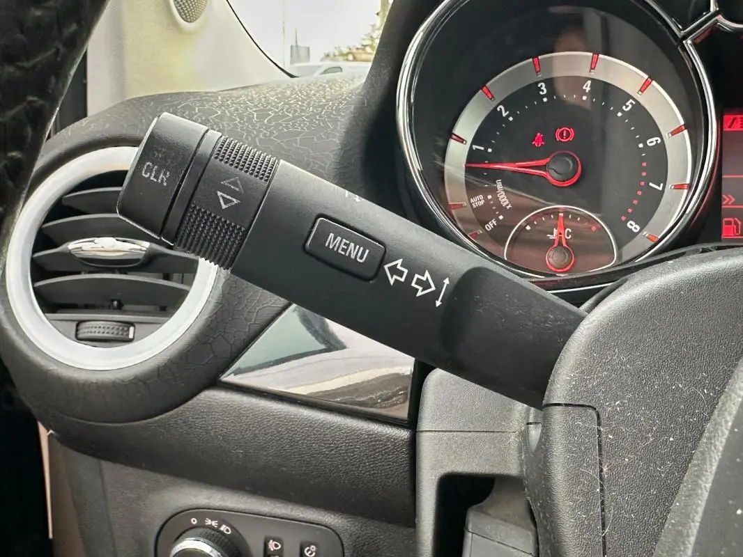 Détail du commodo de clignotant et du tableau de bord avec compte-tours rouge sur Opel Adam marron, vue intérieure côté gauche.