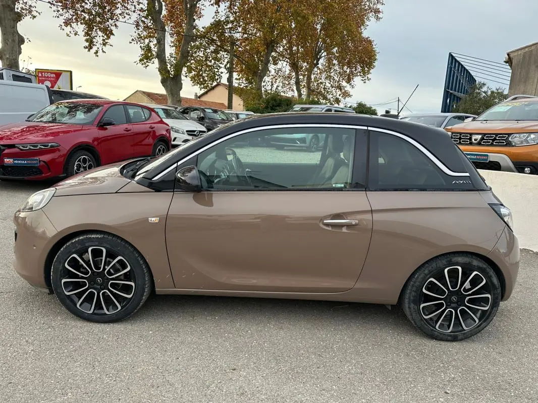 Profil côté gauche d'une Opel Adam marron avec toit noir et jantes alliage 16 pouces, stationnée en extérieur.