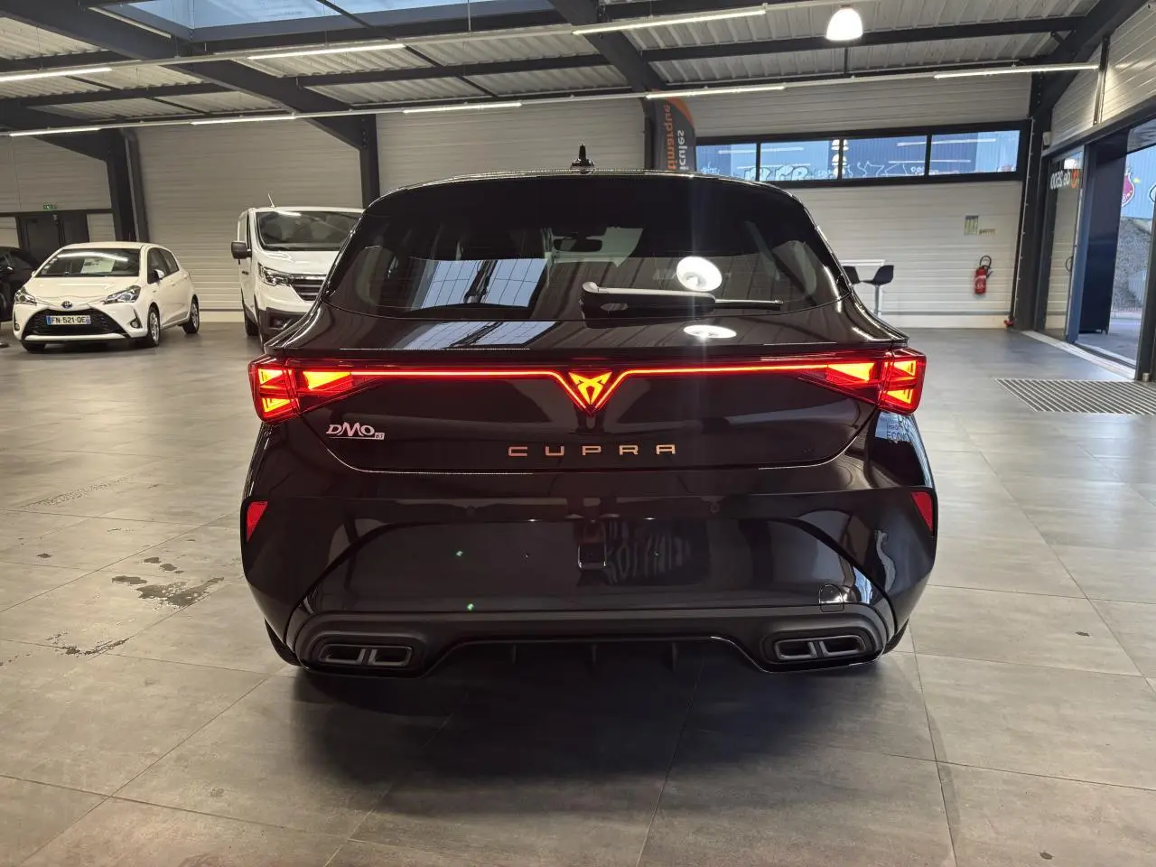 Vue arrière d'une CUPRA Leon noir midnight avec feux arrière Tri-LED allumés et double sortie d'échappement stylisée.