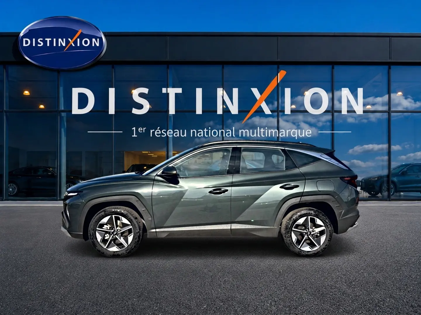 Vue latérale droite d'un Hyundai Tucson vert 2026 hybride avec jantes alu 18 pouces devant une vitrine Distinxion.
