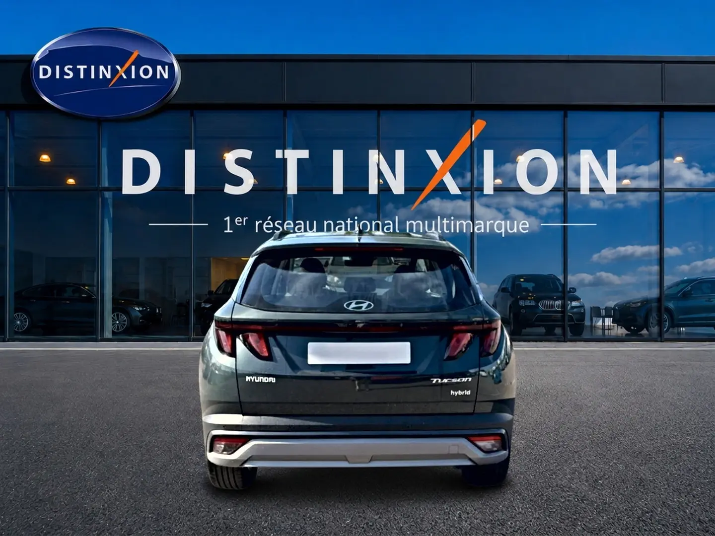 Vue arrière d’un Hyundai Tucson vert hybride 2026, avec feux LED et logo distinctif sur un parking devant un showroom.