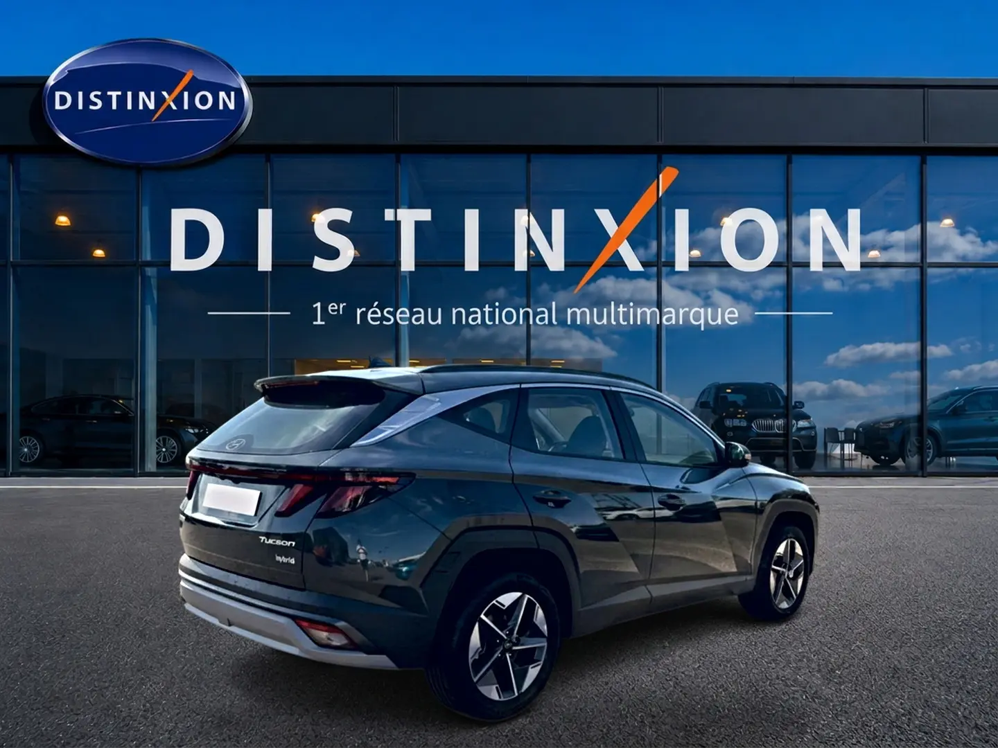 Vue 3/4 arrière droite d'un Hyundai Tucson vert hybride 2026 avec jantes alu et feux arrière LED, devant une vitrine Distinxion.