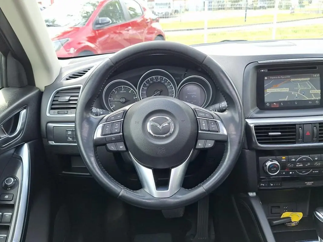 Vue intérieure centrée sur le volant cuir multifonctions et tableau de bord avec écran tactile GPS du Mazda CX-5 gris 2015.