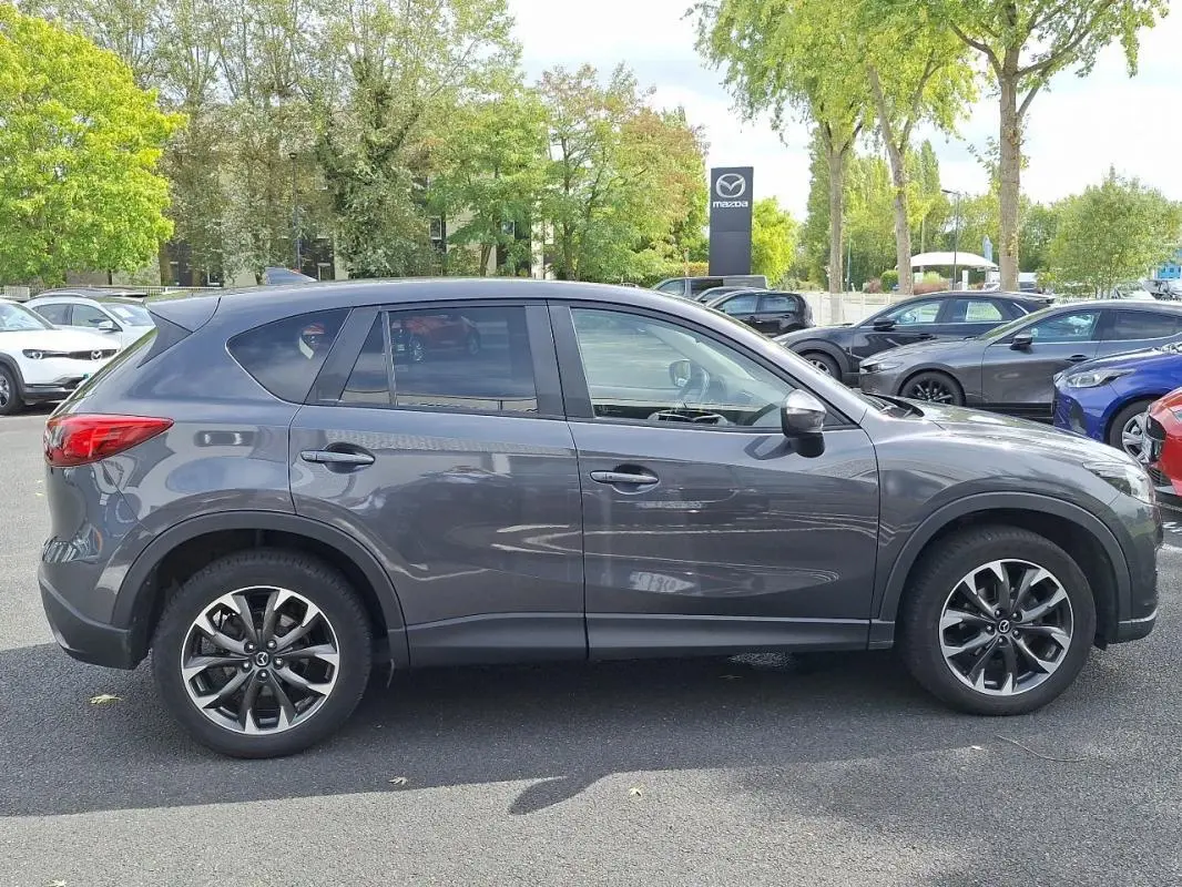 Vue latérale côté gauche d'un Mazda CX-5 gris 2015 avec jantes aluminium et vitres surteintées.