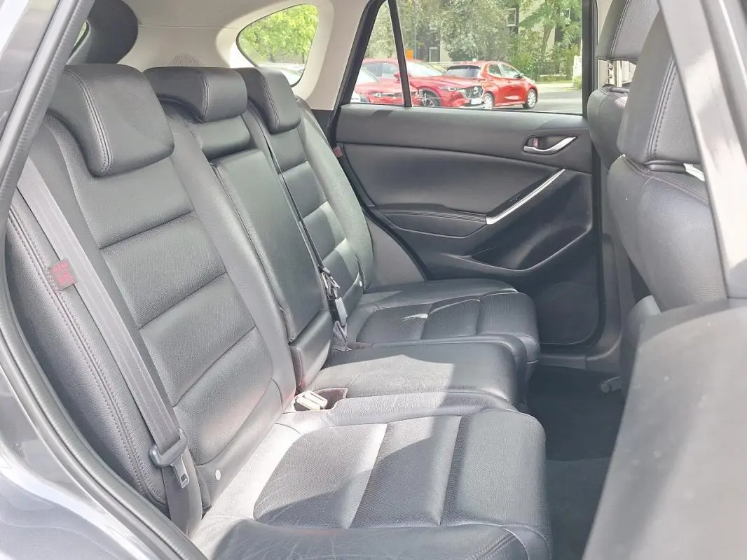 Vue intérieure côté arrière gauche montrant les sièges en cuir noir du Mazda CX-5 gris 2015.