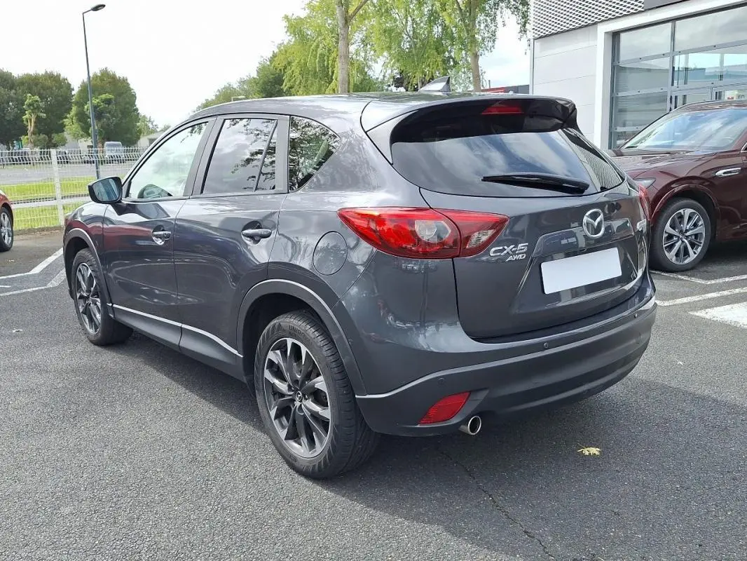 Vue 3/4 arrière droite d'un Mazda CX-5 gris avec jantes aluminium et feux arrière distinctifs sur parking extérieur