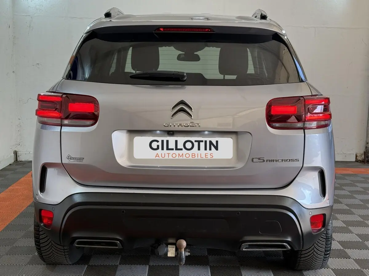 Vue arrière d'un Citroën C5 Aircross gris clair 2023 avec feux LED et attelage visible en intérieur showroom.