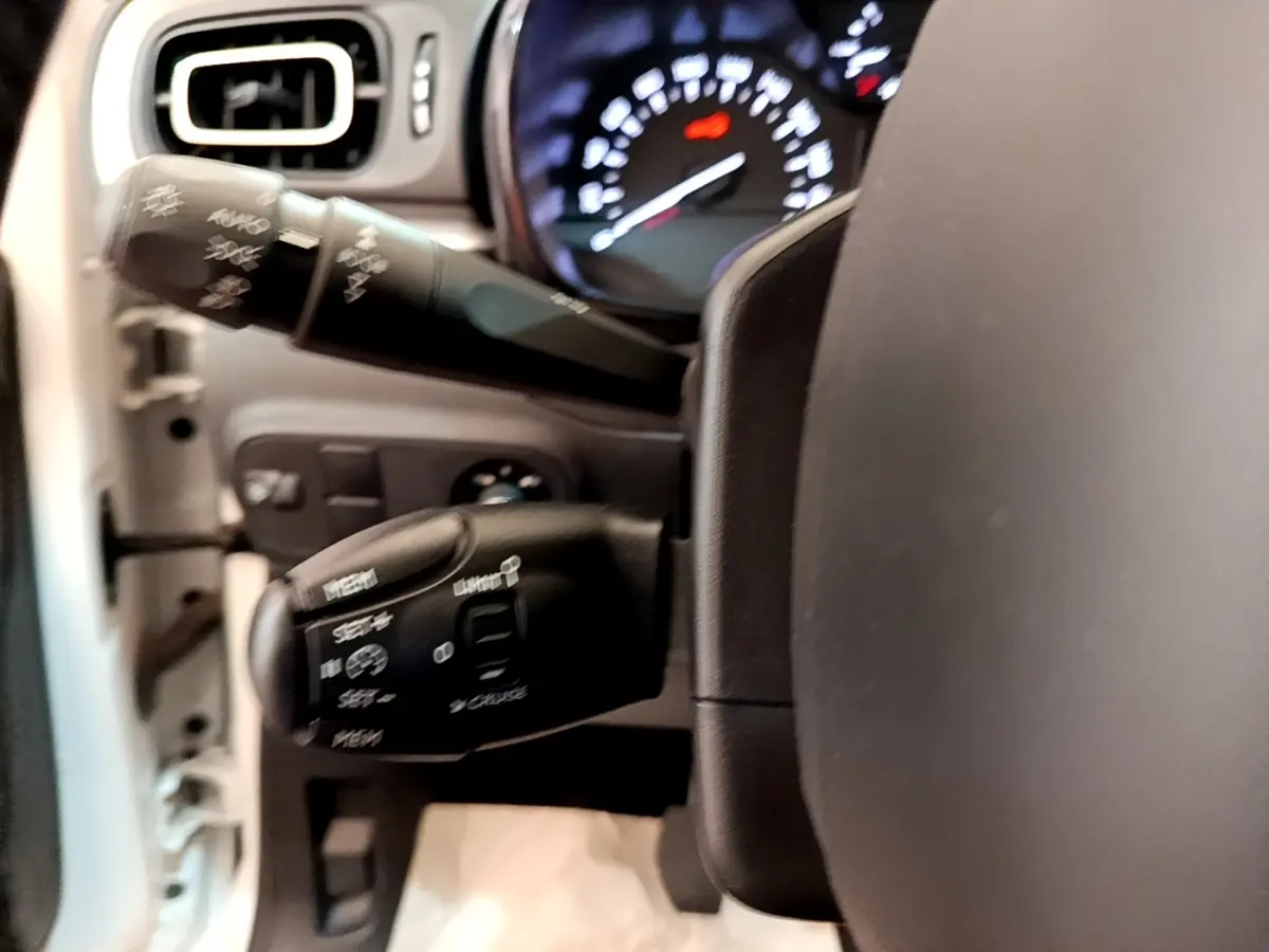 Gros plan sur le volant cuir et les commandes au volant d'une Citroën C3 blanche, tableau de bord lumineux en arrière-plan.
