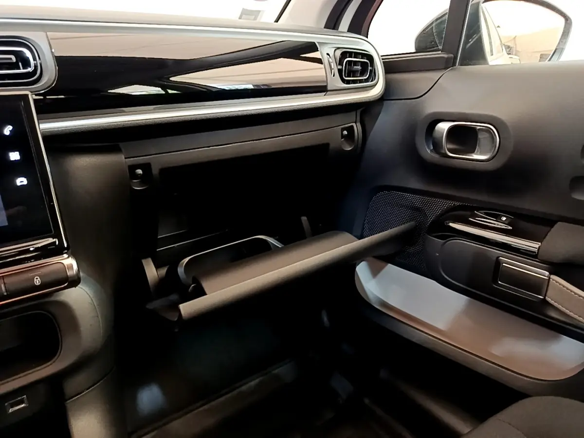 Intérieur de la Citroën C3 blanc, vue côté passager avec boîte à gants ouverte et tableau de bord noir brillant.