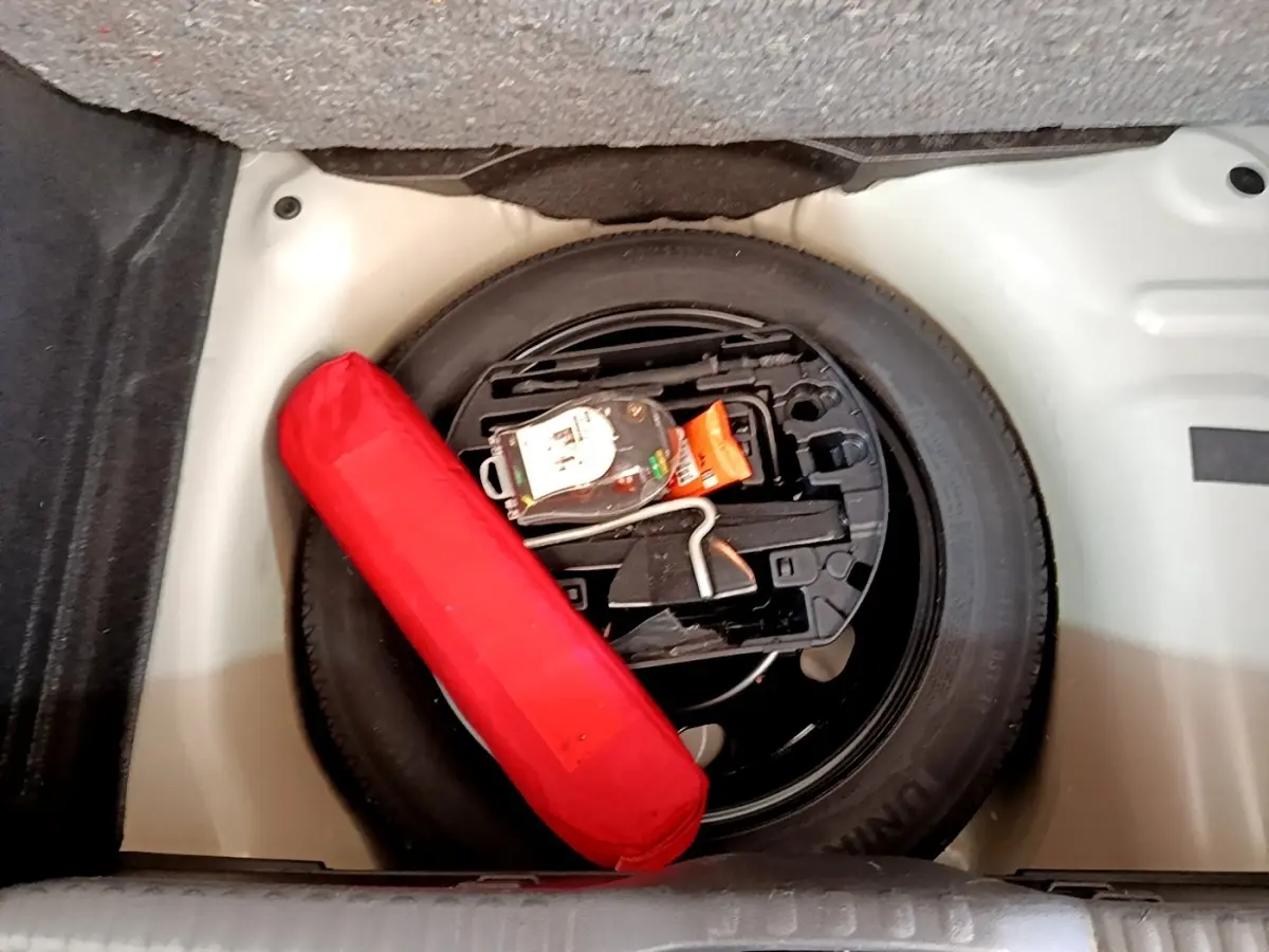 Vue plongeante sur la roue de secours noire et un triangle de signalisation rouge dans le coffre d'une Citroën C3 blanche.